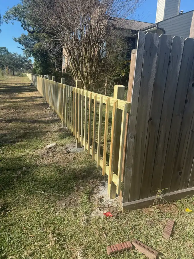 New pressure-treated picket fence meeting an older weathered fence section