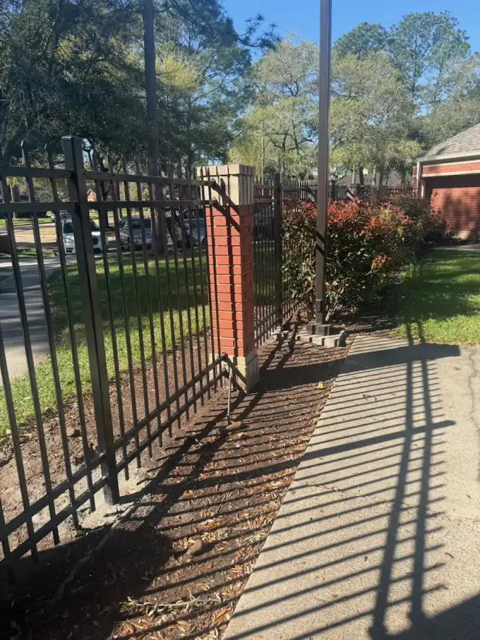 Black ornamental iron fence on brick columns with automated gate approach