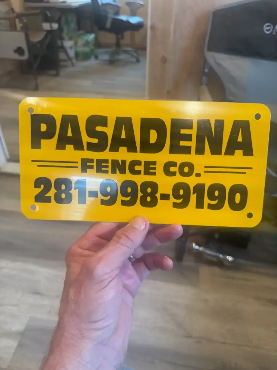 The Pasadena Fence Co. yard sign: yellow plate with black lettering reading Pasadena Fence Co. 281-998-9190