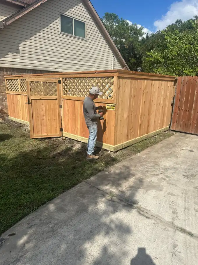 Pasadena Fence Co. crew member fixing the company sign to a finished cedar and lattice enclosure